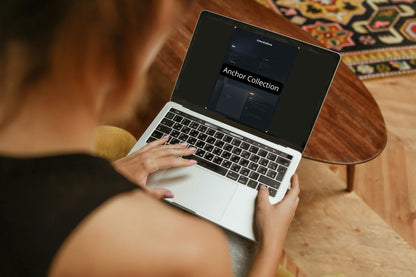 Person using a laptop with 'Anchor Collection' on the screen, sitting at a wooden table.