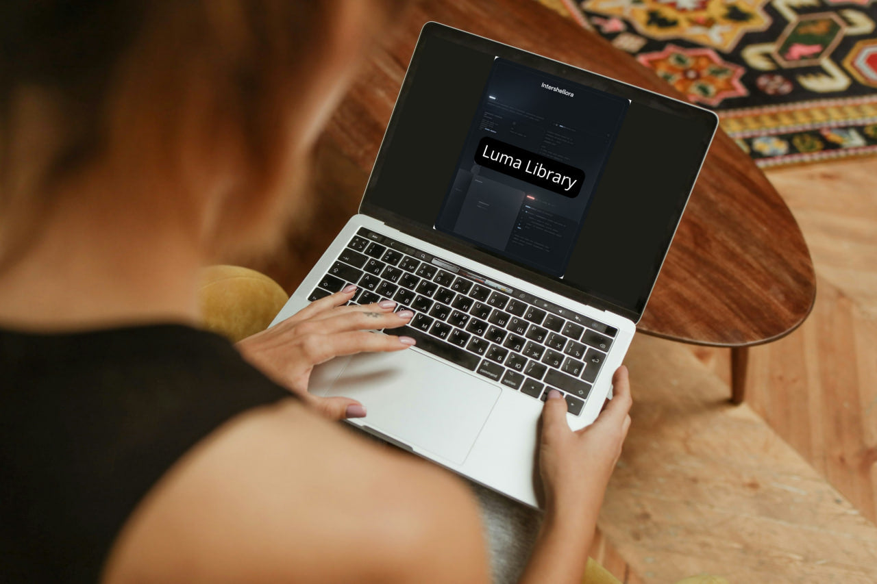 Person using a laptop with 'Luma Library' on the screen, sitting at a wooden table.